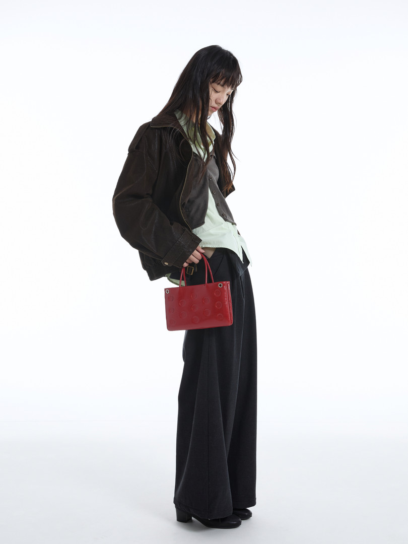 Model wearing a dark jacket and wide-leg pants while holding a small red handbag