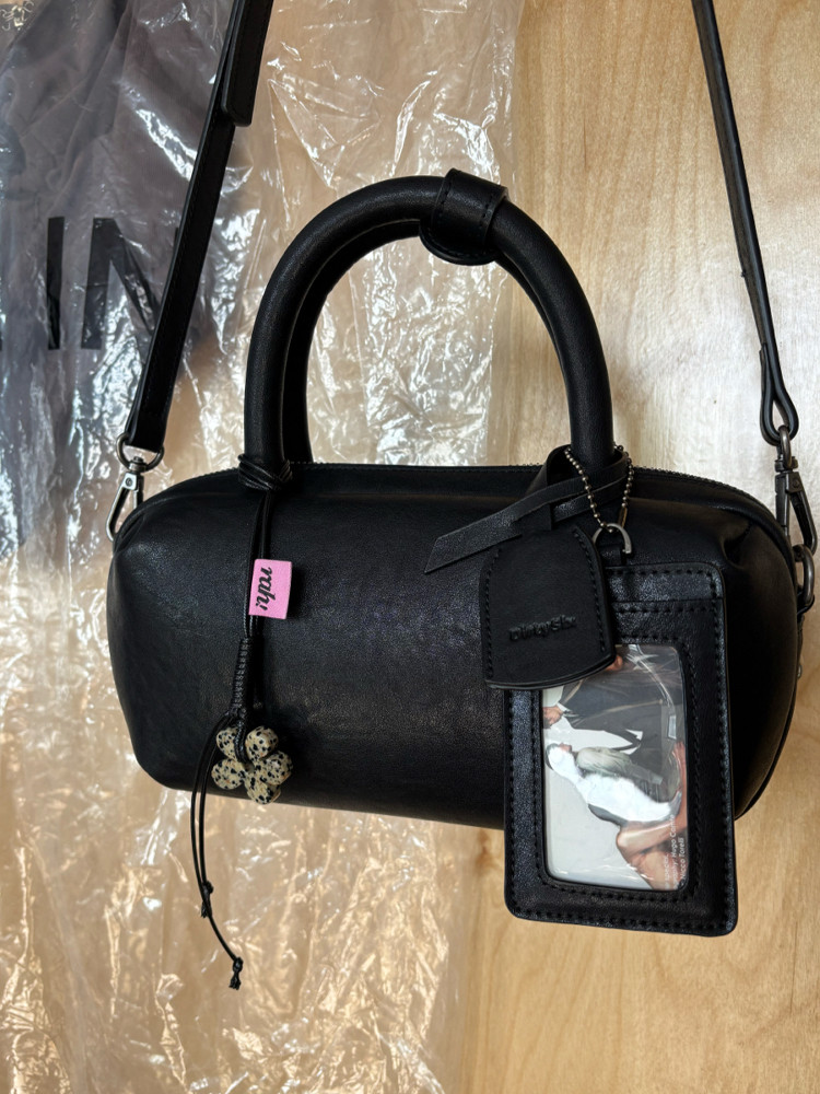 Black leather handbag with top handle, shoulder strap, and hanging tag accessories