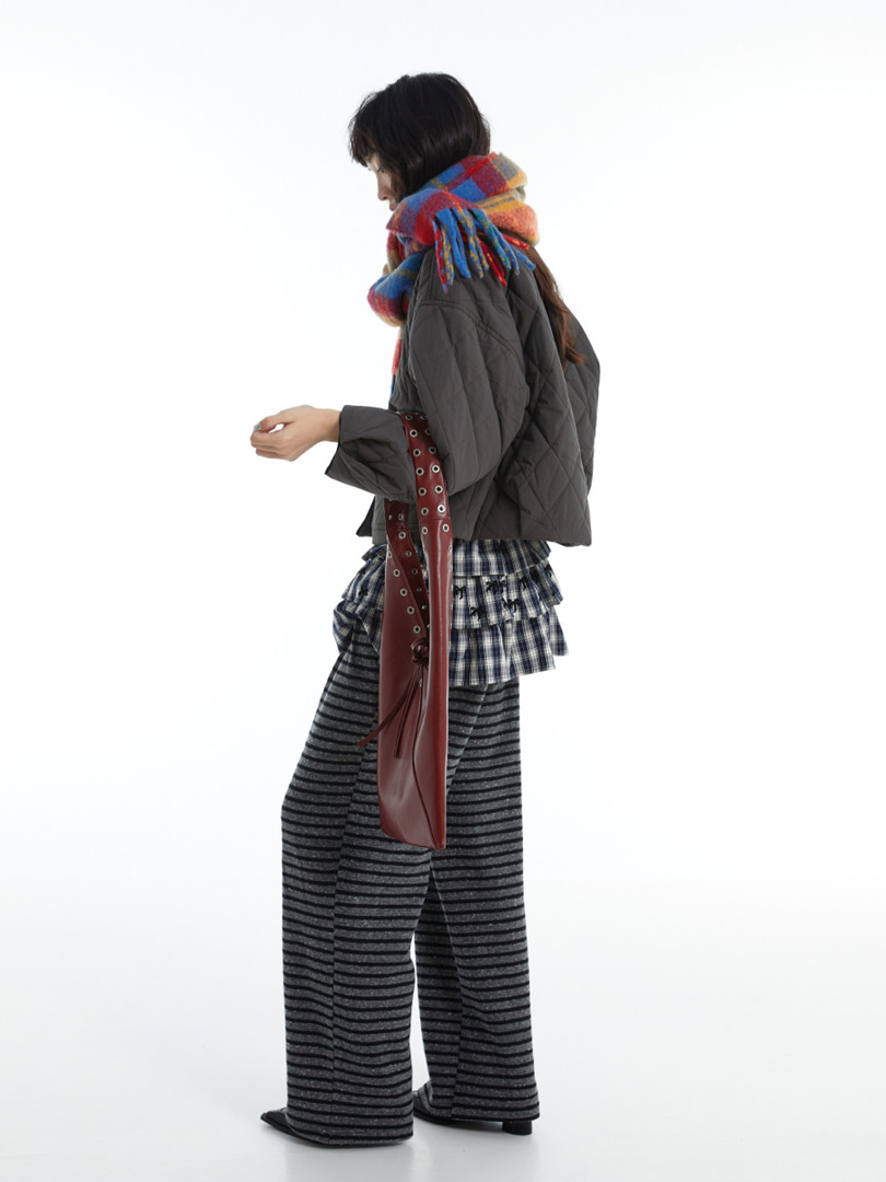Model wearing a layered winter outfit with a plaid scarf, cropped jacket, and striped pants