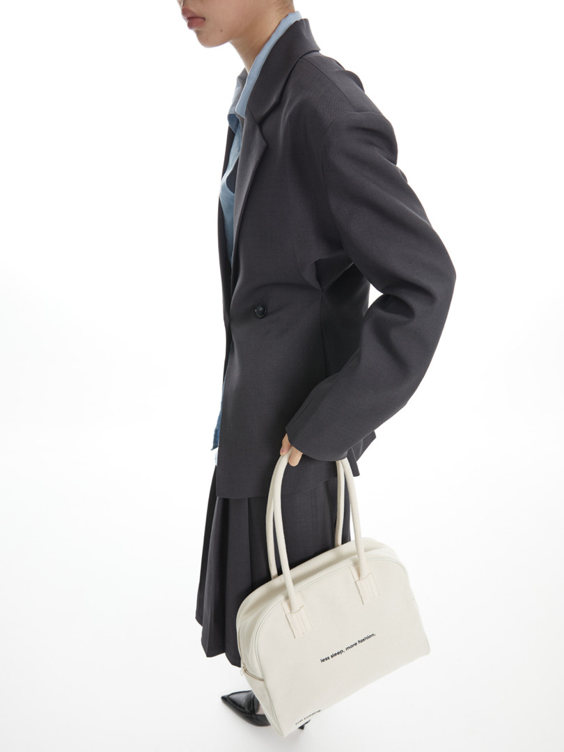 Model wearing a dark tailored blazer and holding a cream tote bag on a white background