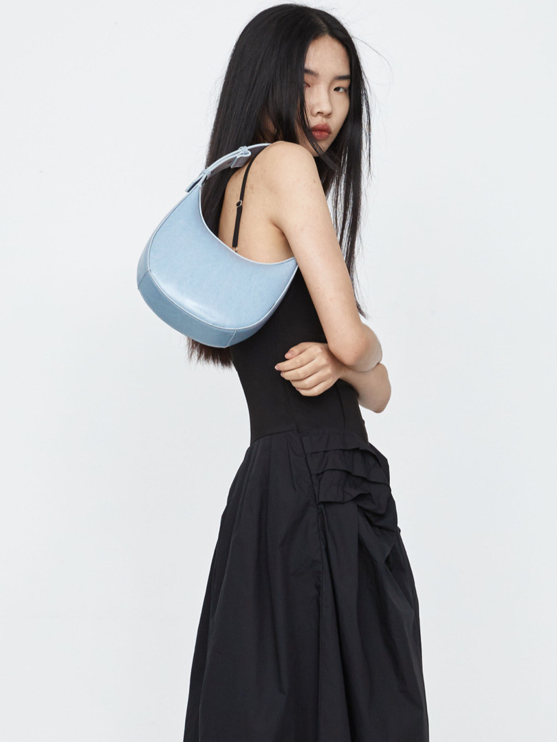 Model wearing a black sleeveless dress with a light blue shoulder bag