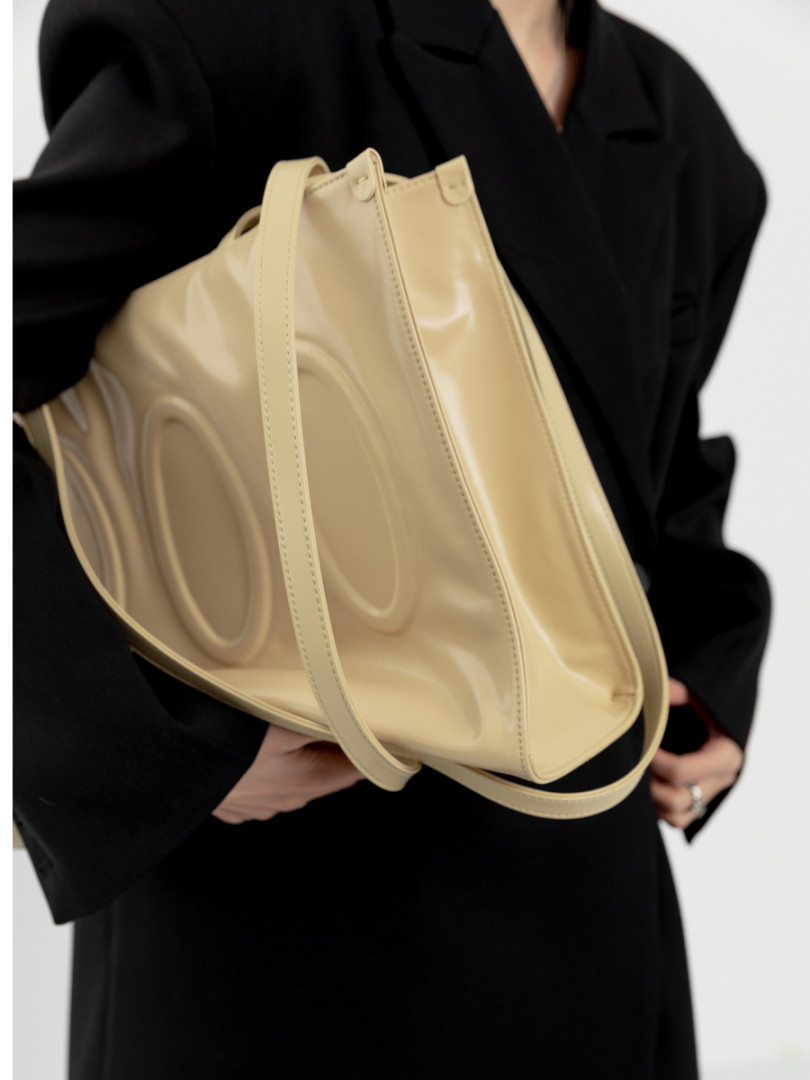 Beige structured tote handbag held by a model in a black outfit