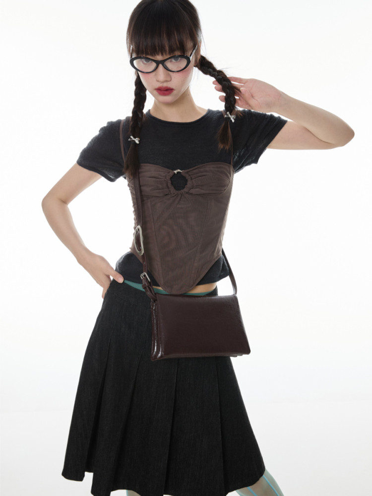Fashion model wearing a black top with a brown corset-style overlay and matching shoulder bag