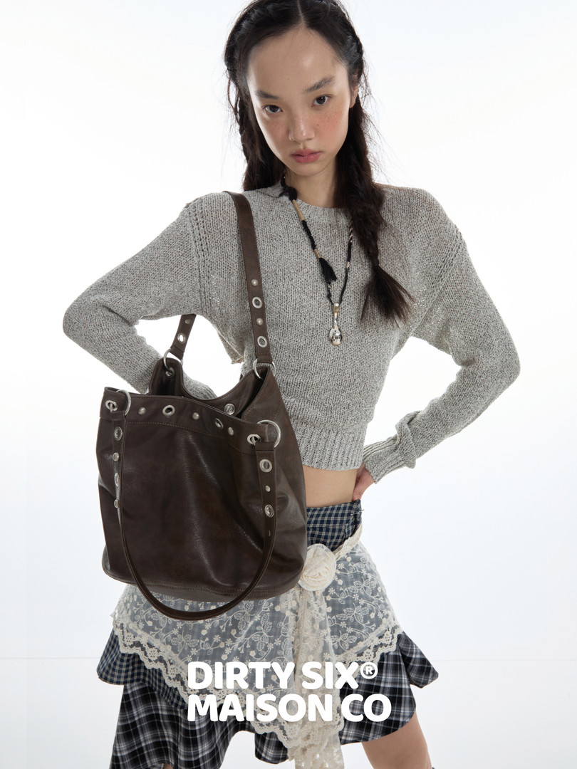 Model wearing a gray knit sweater with a brown leather shoulder bag and layered plaid skirt outfit