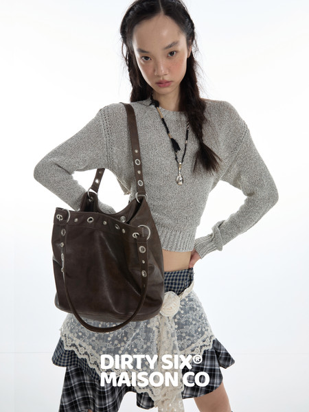 Model wearing a gray knit sweater with a brown leather shoulder bag and layered plaid skirt outfit