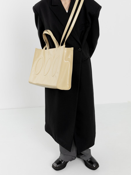 Cream tote bag worn over a black long coat on a model