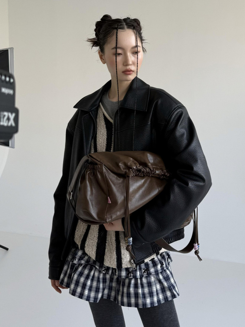 Model wearing a black leather jacket with a plaid mini skirt and brown shoulder bag