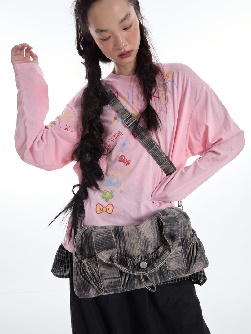 Model wearing a pink graphic long-sleeve top with a gray crossbody bag