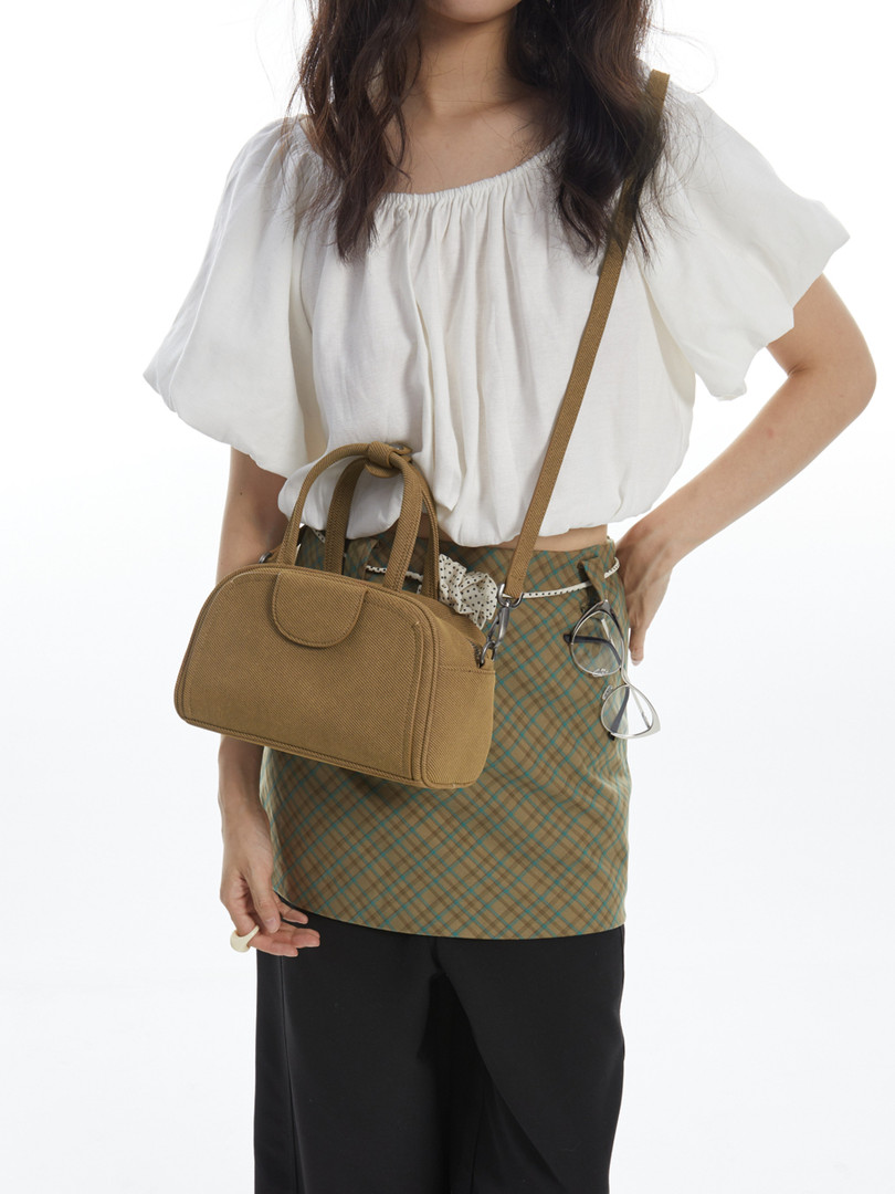 Model wearing a tan crossbody handbag with a white blouse and plaid skirt