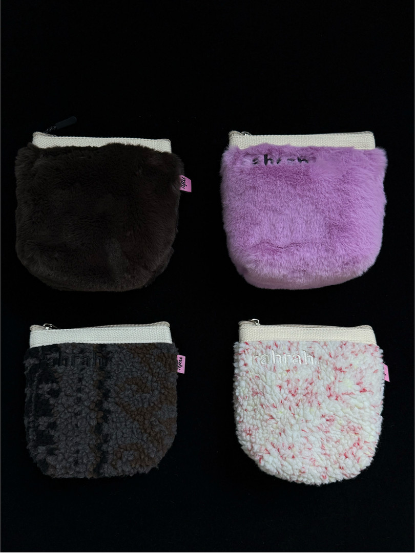 Four fuzzy faux-fur zip pouches in black, purple, gray, and white on a black background