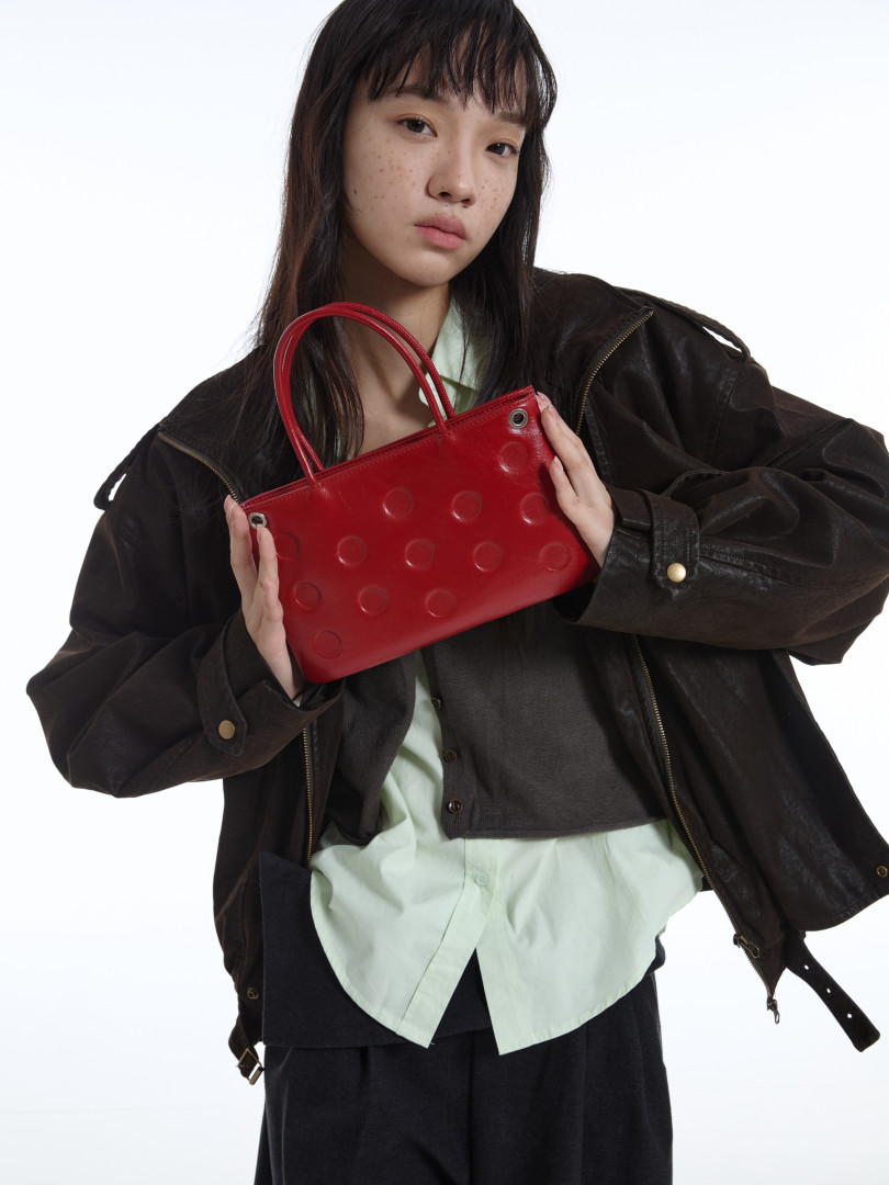 Red handbag held by a model wearing layered dark clothing