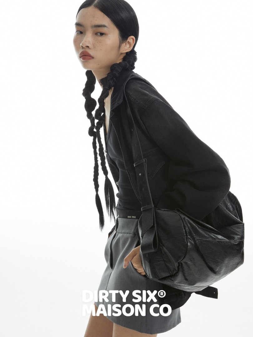 Model wearing black jacket and carrying a black leather bag on a white background