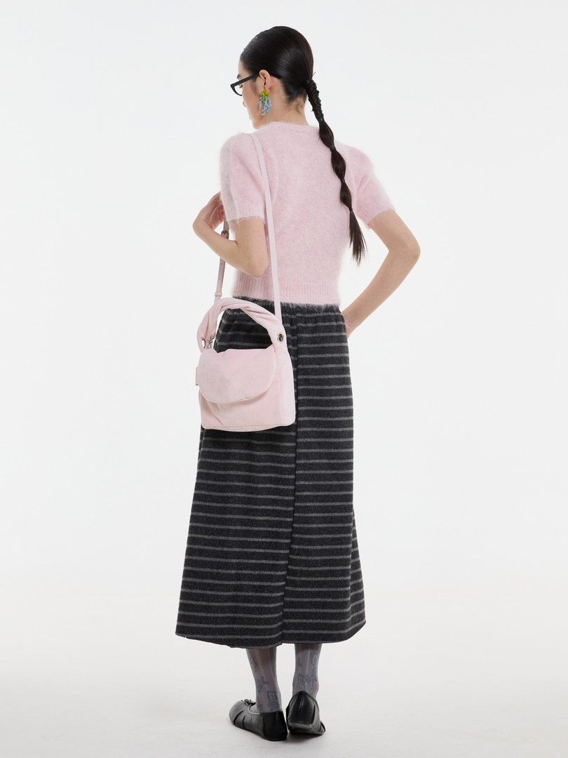 Model wearing a pink fuzzy short-sleeve top with a black striped wide-leg skirt and a pale pink shoulder bag
