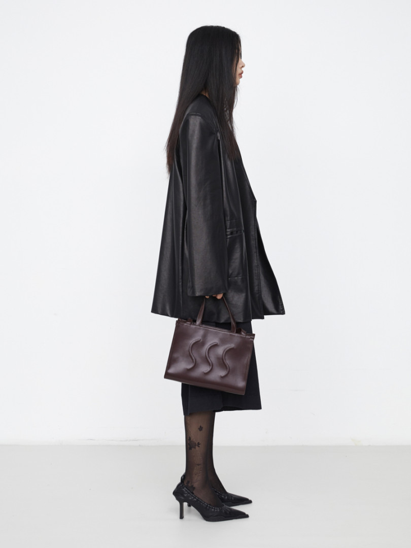 Model wearing a black coat and holding a brown leather handbag
