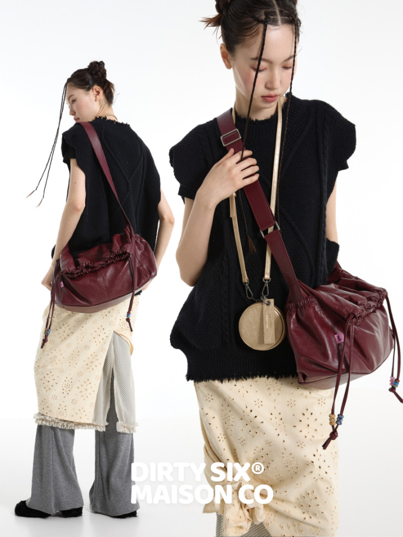 Fashion model wearing a black textured top with a burgundy crossbody bag and layered skirt/pants look