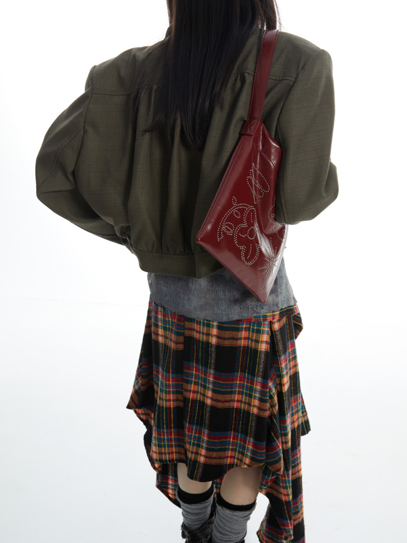 Model wearing an olive jacket with a plaid skirt and red shoulder bag