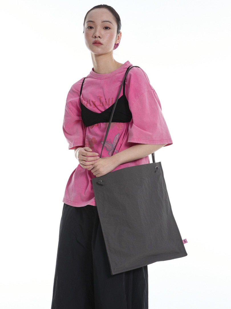 Model wearing a pink oversized tee and carrying a large dark gray tote bag