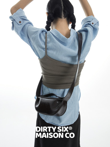 Model wearing a light blue shirt with a black shoulder bag on a white background
