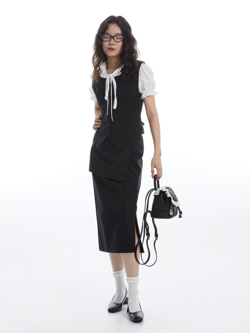 Female model wearing a black midi dress layered over a white puff-sleeve blouse, holding a small black backpack