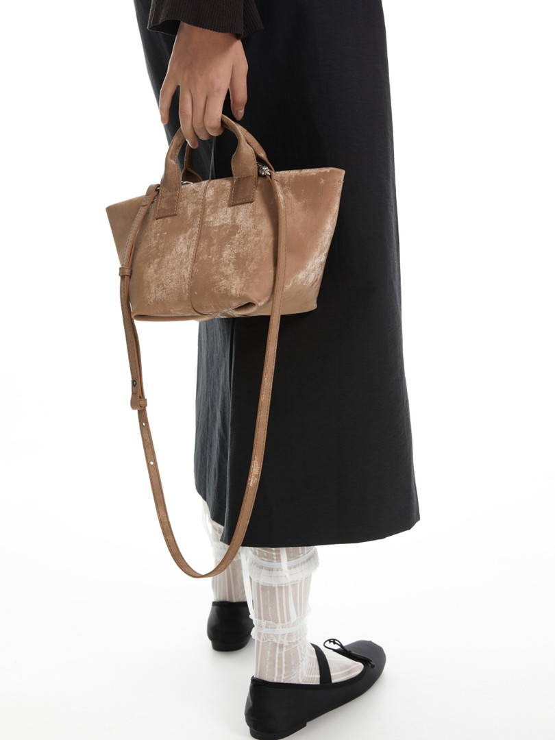 Brown leather handbag held by a model on a white background
