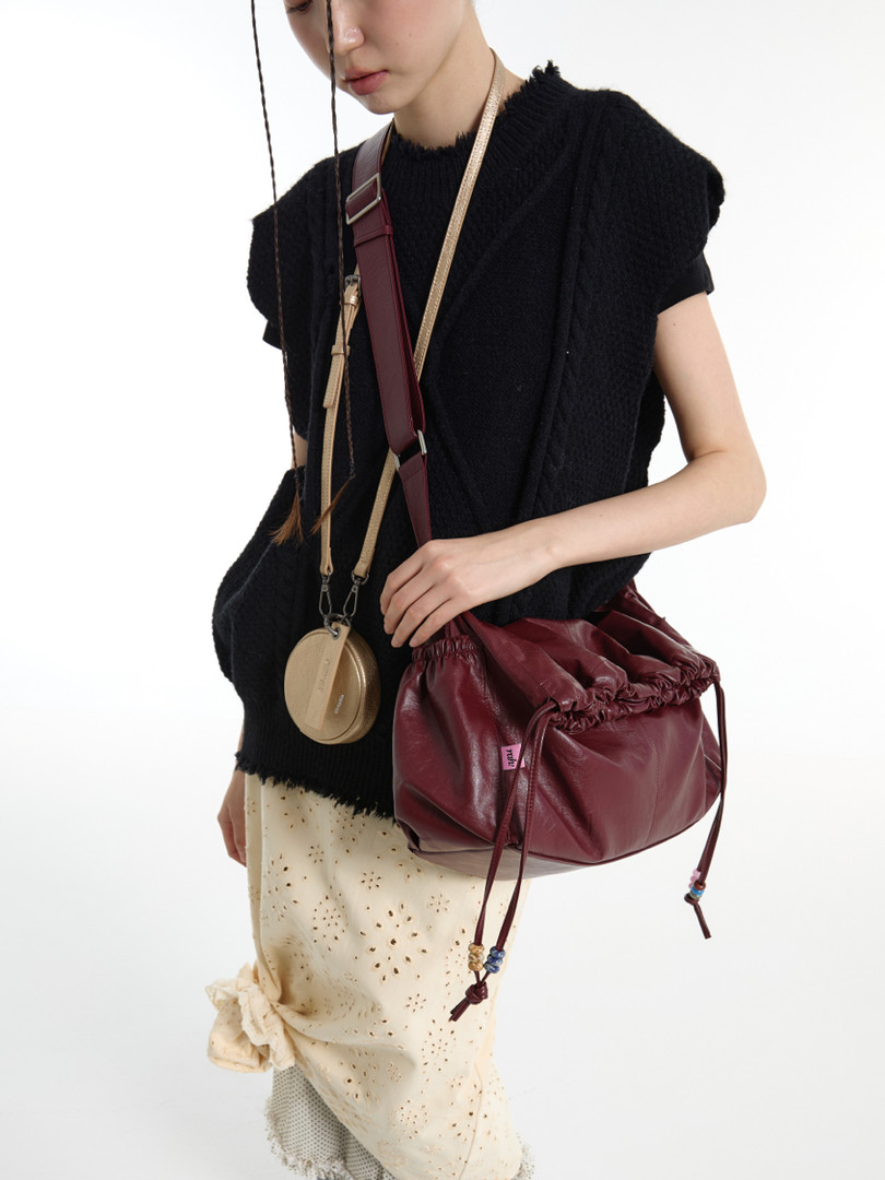 Model wearing a black sleeveless top with a burgundy drawstring shoulder bag