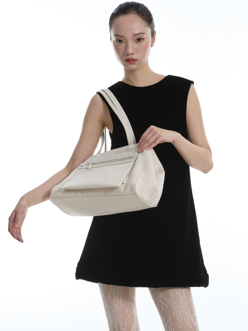 Model wearing a black sleeveless dress and carrying a white shoulder bag