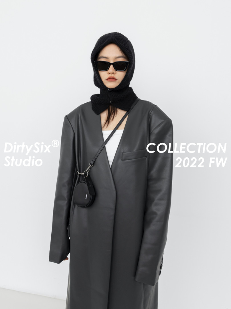 Model wearing a black faux leather long coat with hood and crossbody bag