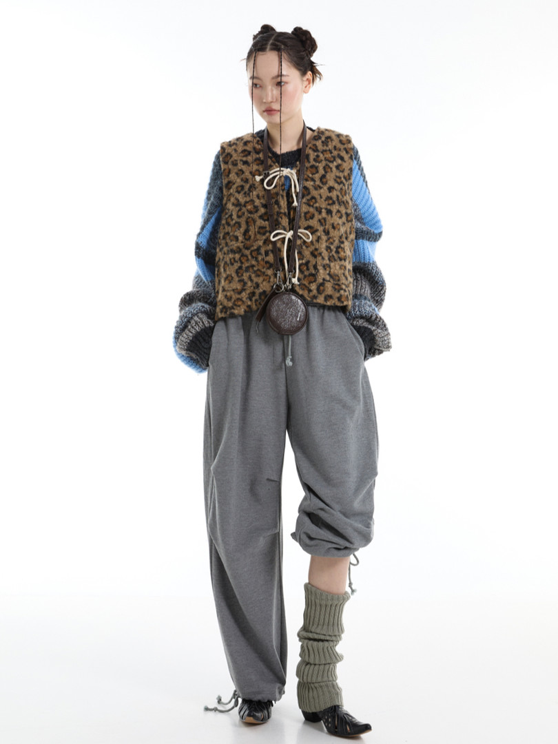 Fashion model wearing a layered street-style outfit with a leopard print vest, striped sweater, and gray pants