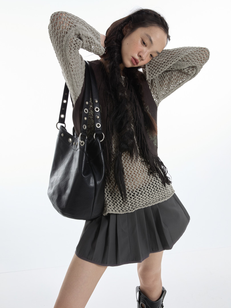 Fashion model wearing a mesh knit top, pleated black skirt, and black shoulder bag