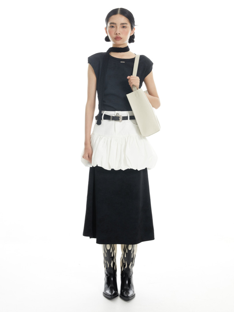 Model wearing a black-and-white fashion outfit with boots and a tote bag on a white background