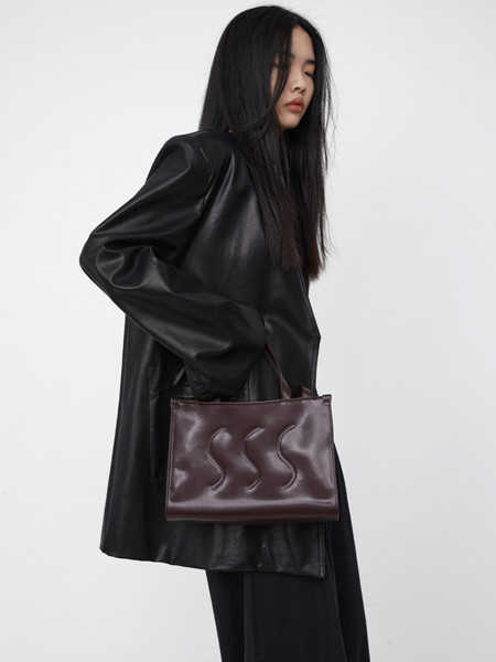 Brown leather tote bag worn by a model with a black leather coat