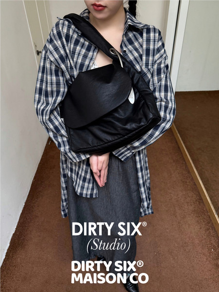 Black leather shoulder bag worn crossbody by a model in a plaid shirt