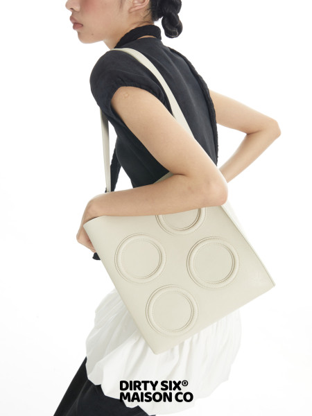 Model wearing a cream shoulder tote bag with circular stitched details