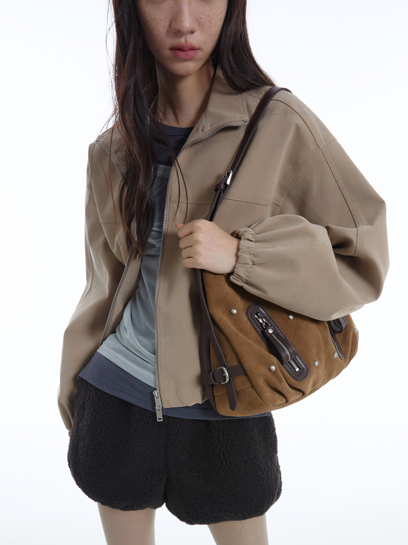 Model wearing a beige zip-up jacket and carrying a brown shoulder bag