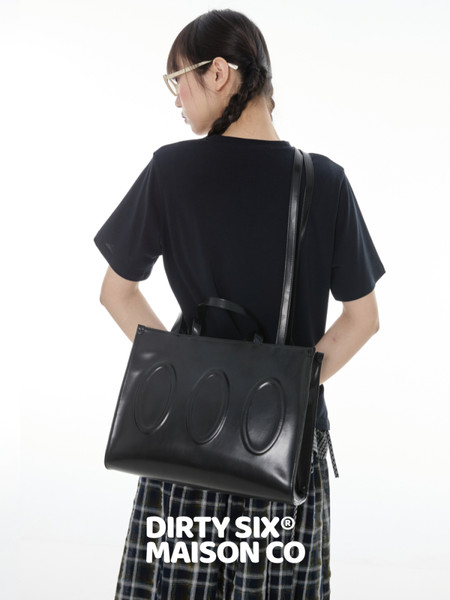 Black leather tote bag worn by a model with a casual outfit