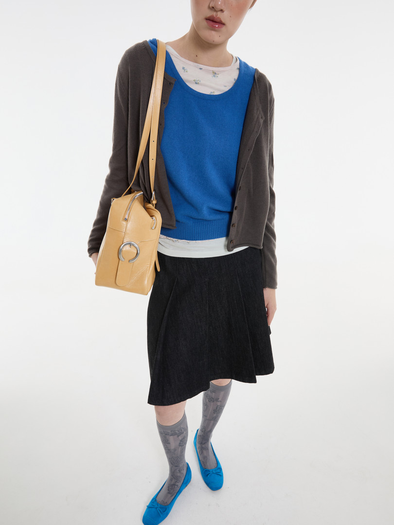 Model wearing a blue top, dark cardigan, black skirt, and tan shoulder bag