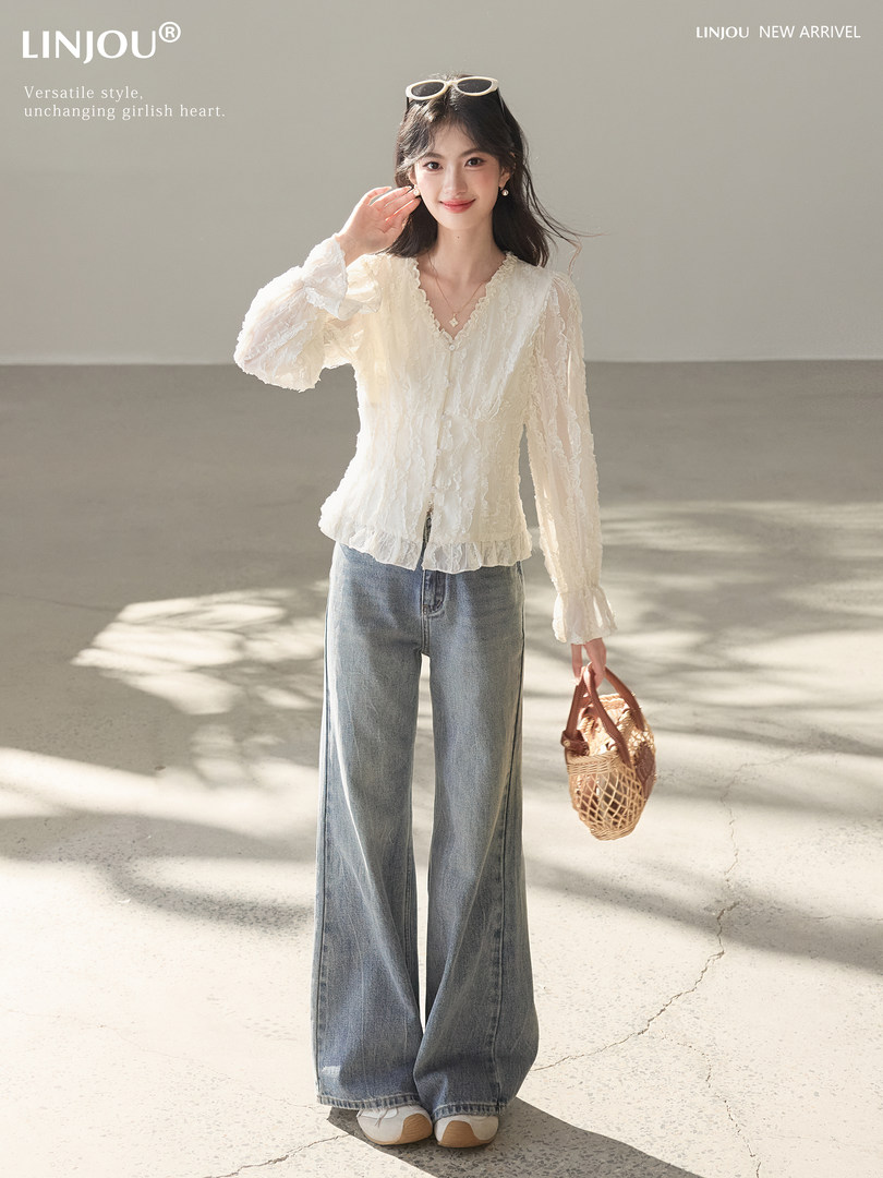 Model wearing a white lace blouse with wide-leg blue jeans and a woven handbag