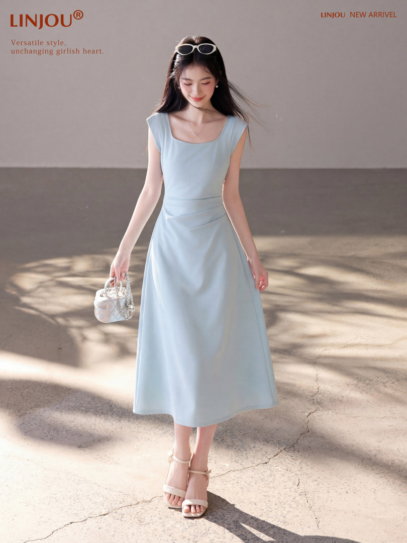 Model wearing a light blue sleeveless midi dress with a small handbag
