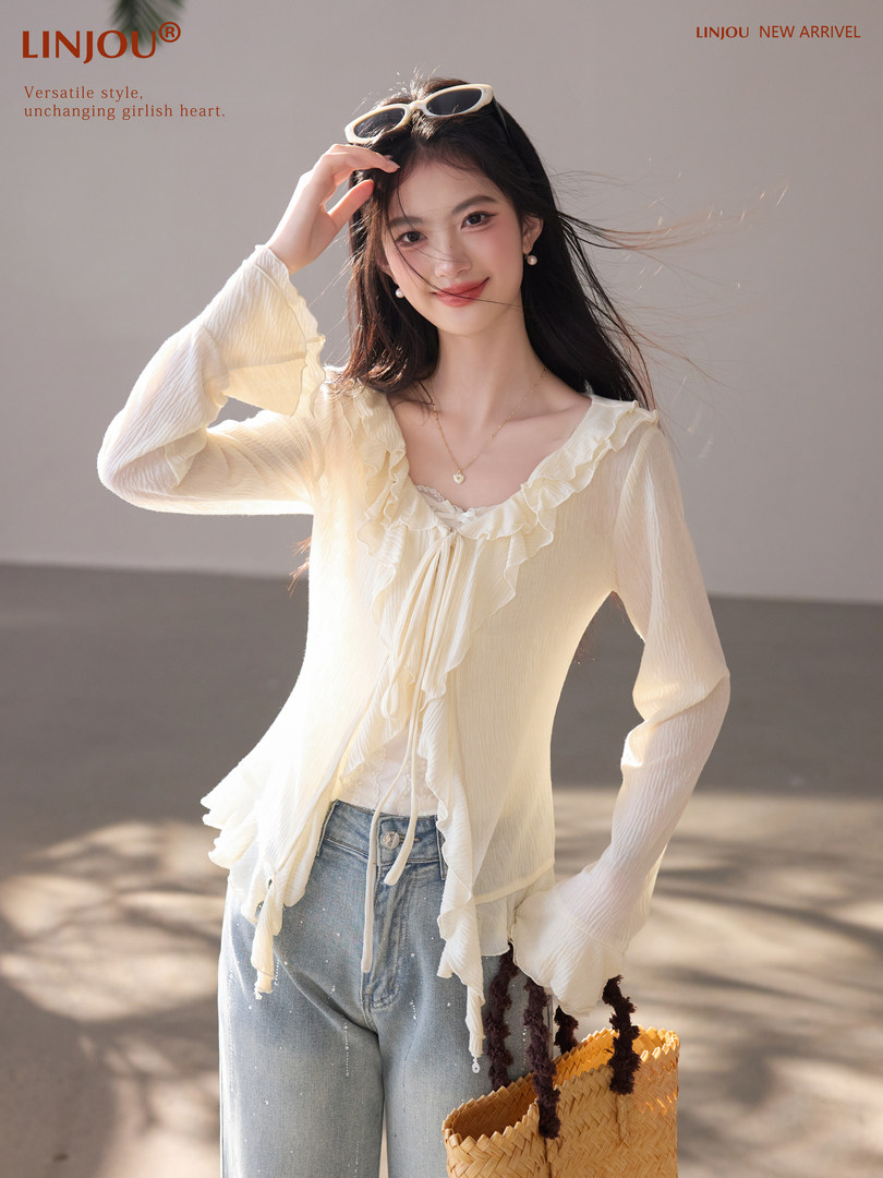Model wearing a cream ruffled blouse with jeans and a straw bag