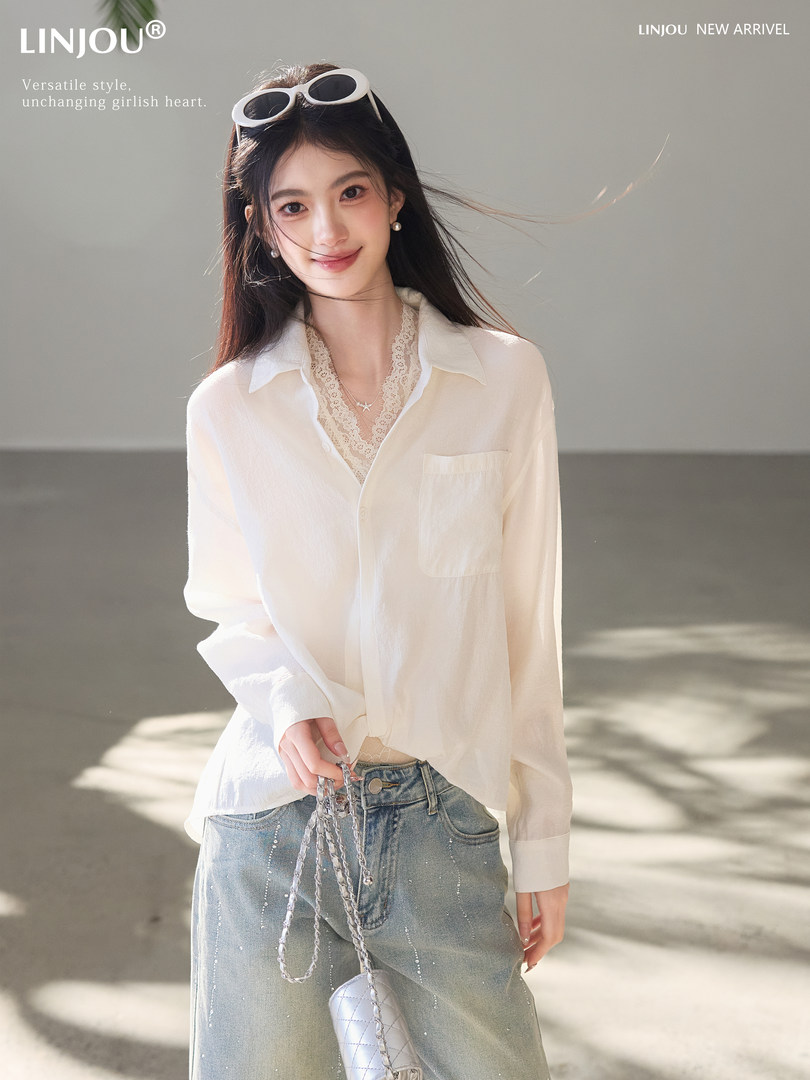 Model wearing a white sheer button-up blouse with light blue jeans and a chain bag