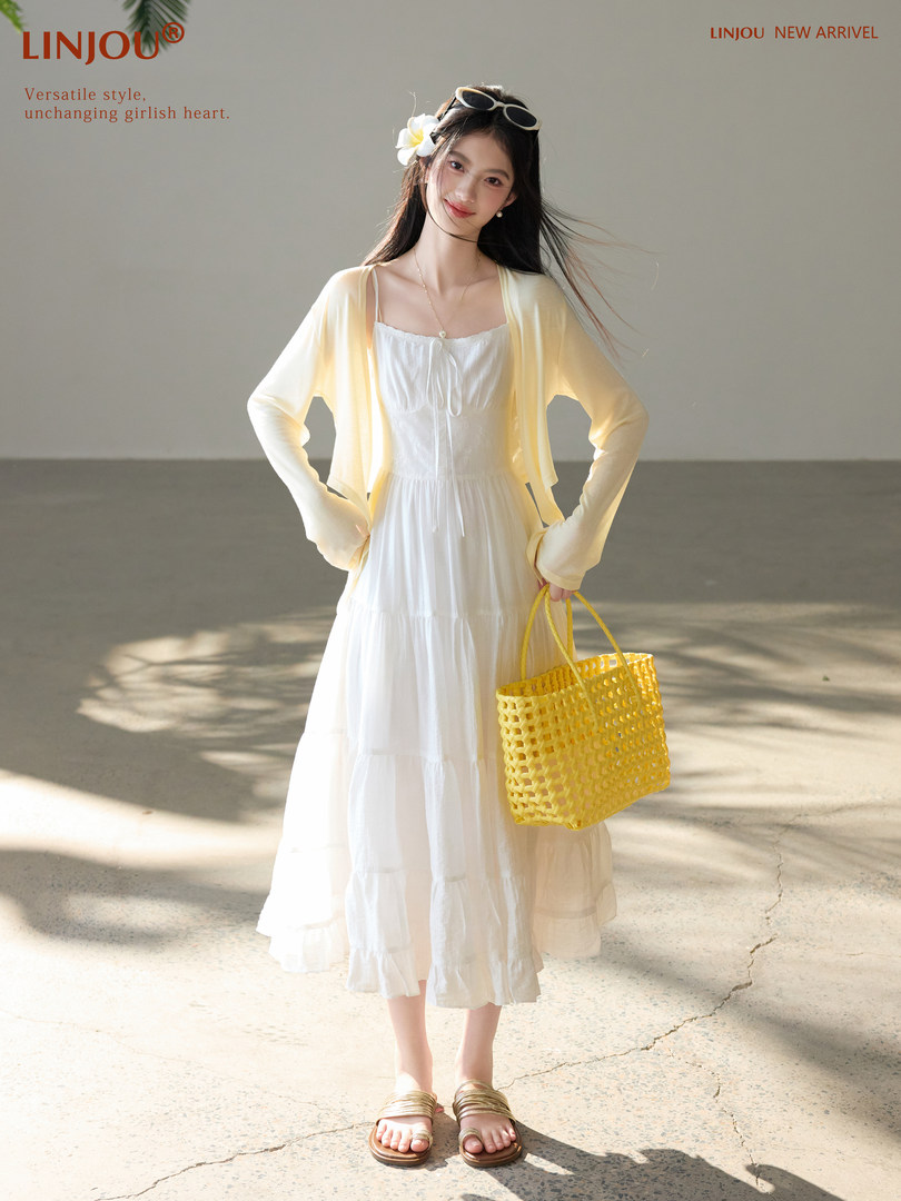 Woman wearing a white midi dress with a light yellow cardigan, holding a woven yellow tote bag