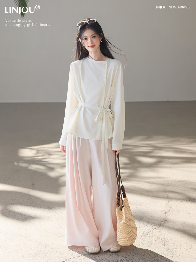 Woman wearing a white belted blouse with soft pink wide-leg pants and a woven straw bag