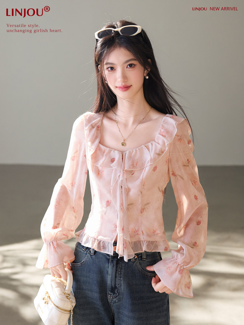 Model wearing a pink floral ruffled blouse with long sleeves and a small handbag
