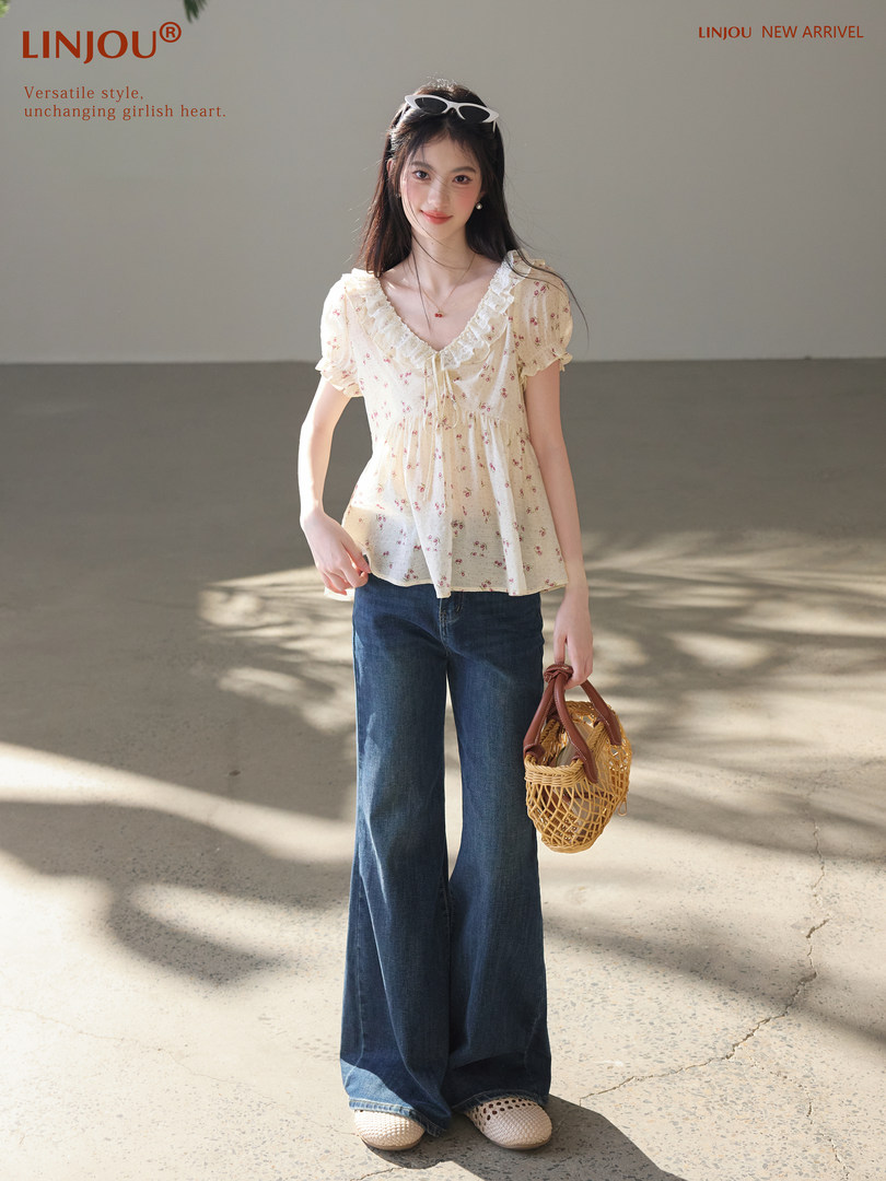 Model wearing a cream floral ruffle blouse with wide-leg jeans and a woven handbag