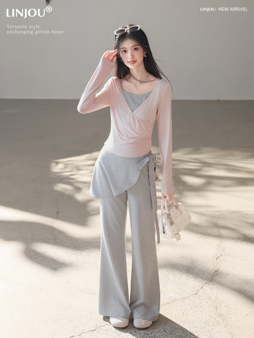 Model wearing a light pink wrap top with gray wide-leg lounge pants and a small handbag