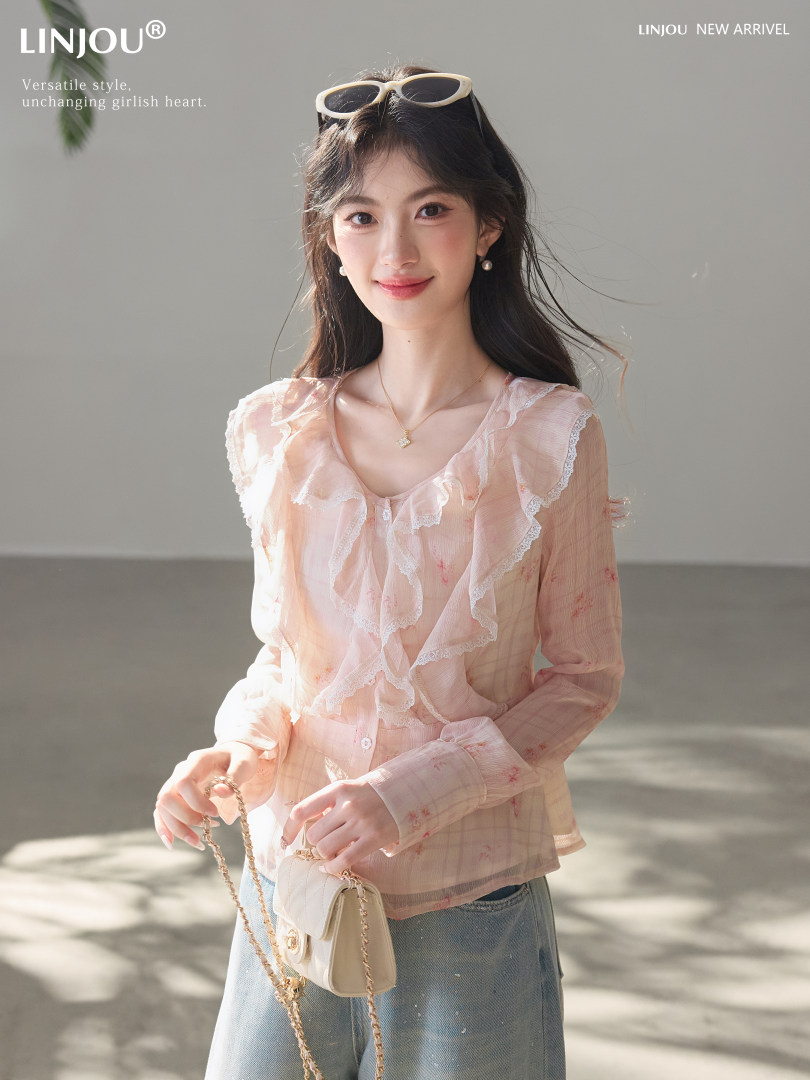 Model wearing a light pink ruffled sheer blouse with a small shoulder bag