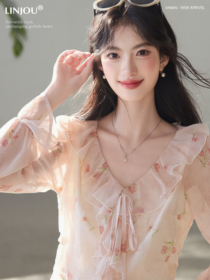 Model wearing a light pink floral ruffle blouse with a tie front