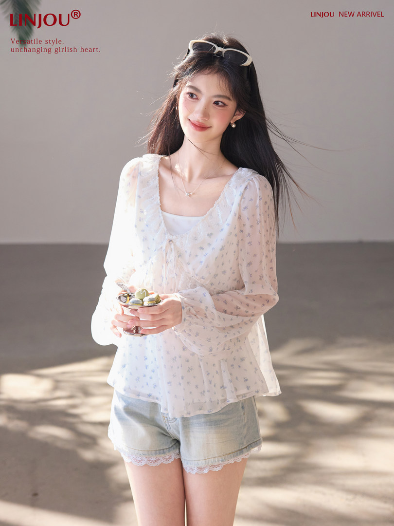 Model wearing a sheer floral blouse with light denim shorts