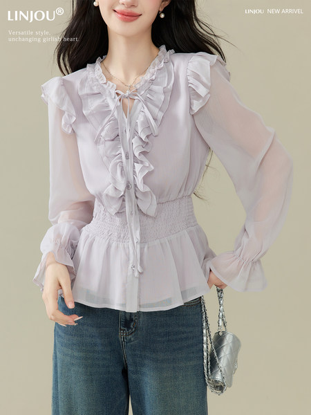Model wearing a light sheer ruffled blouse with long sleeves and tie front