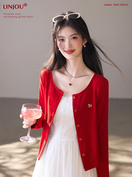 Woman wearing a red cardigan over a white dress, holding a drink